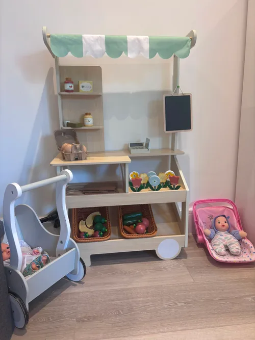 A wooden market stall with pretend produce, alongside a doll pram