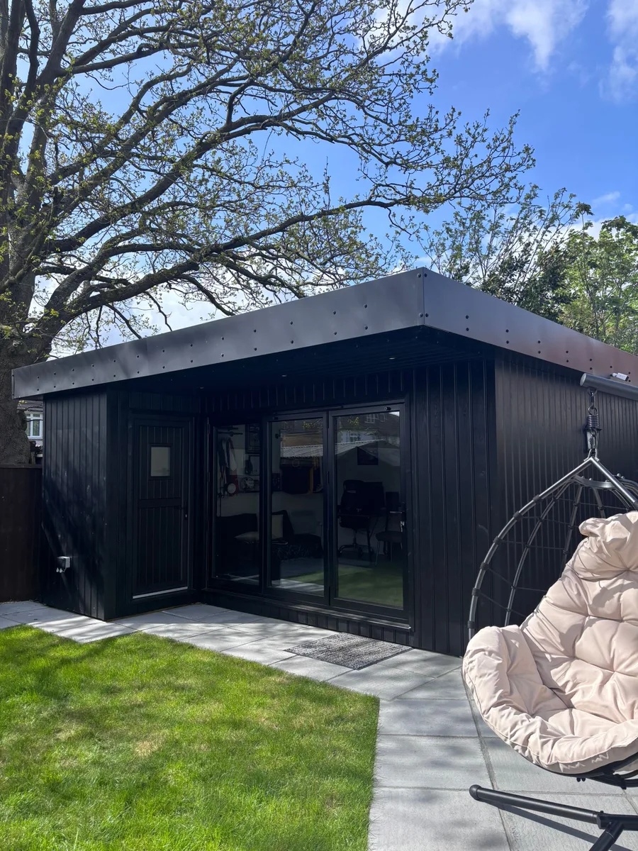 The purpose-built garden outbuilding under a tree, with bi-fold doors and an egg chair