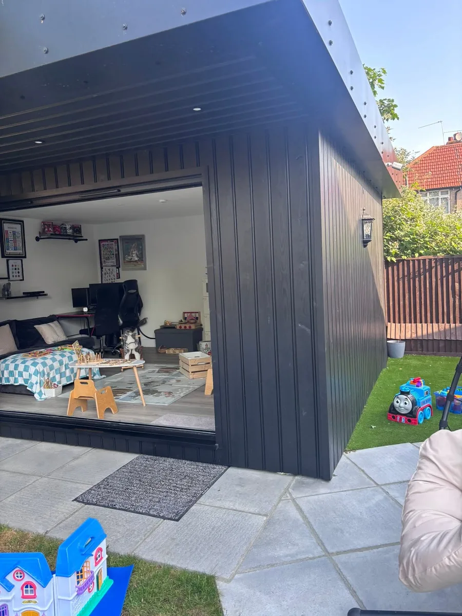 The purpose-built garden outbuilding under a tree, with bi-fold doors and an egg chair