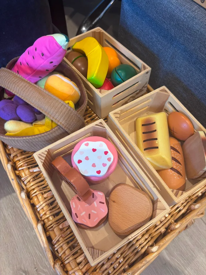 A picnic basket of wooden play food: bread, fruit, ice cream and pastries