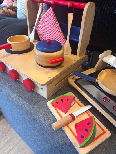 A wooden play kitchen with pots, pans and a toy watermelon to slice